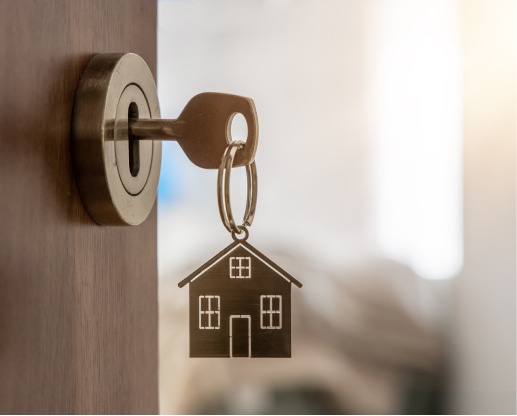 Esecuzioni Mobiliari e Immobiliari. La chiave inserita in una serratura, con un portachiavi a forma di casa che pende dal suo anello, simboleggia l'ingresso in un'abitazione.